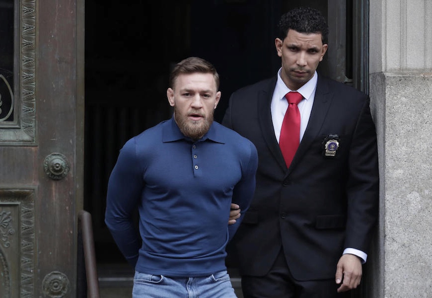 Ultimate fighting star Conor McGregor, left, is led by an official to an unmarked vehicle while leaving the 78th Precinct of the New York Police Department, Friday, April 6, 2018, in the Brooklyn borough of New York. McGregor is facing criminal charges in the wake of a backstage melee he allegedly instigated that has forced the removal of three fights from UFC's biggest card of the year. Video footage appears to show the promotion's most bankable star throwing a hand truck at a bus full of fighters after a Thursday news conference for UFC 223 at Brooklyn's Barclays Center. (AP Photo/Julio Cortez)